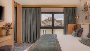 Habitación de hotel moderna con una cama grande, un escritorio y vistas de la ciudad a través de amplios ventanales.