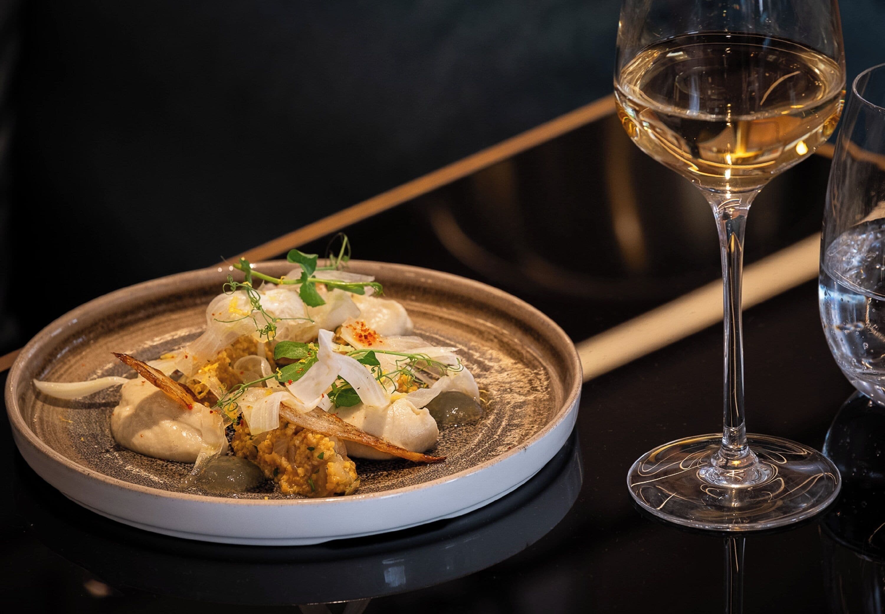A plate of food with a glass of white wine on a table.