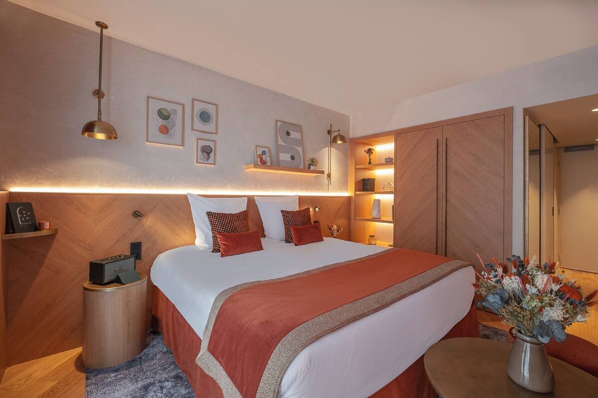 Ein modernes Schlafzimmer mit einem großen Bett, Nachttischen, einer Nachttischlampe, einem an der Wand befestigten Regal mit Dekoration und einem Spiegel.