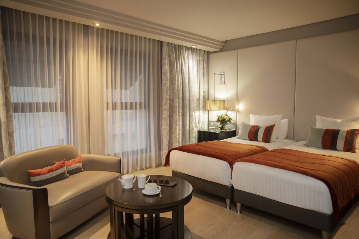 Ein Hotelzimmer mit einer Couch, einem runden Tisch mit einer Serviertablett voller Speisen, einem Bett mit zwei Kissen und einem Nachttisch mit einer Lampe.