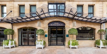 Entrada de un hotel con fachada clásica, puerta de cristal y un letrero que dice 'HOTEL BURDI GALA'.
