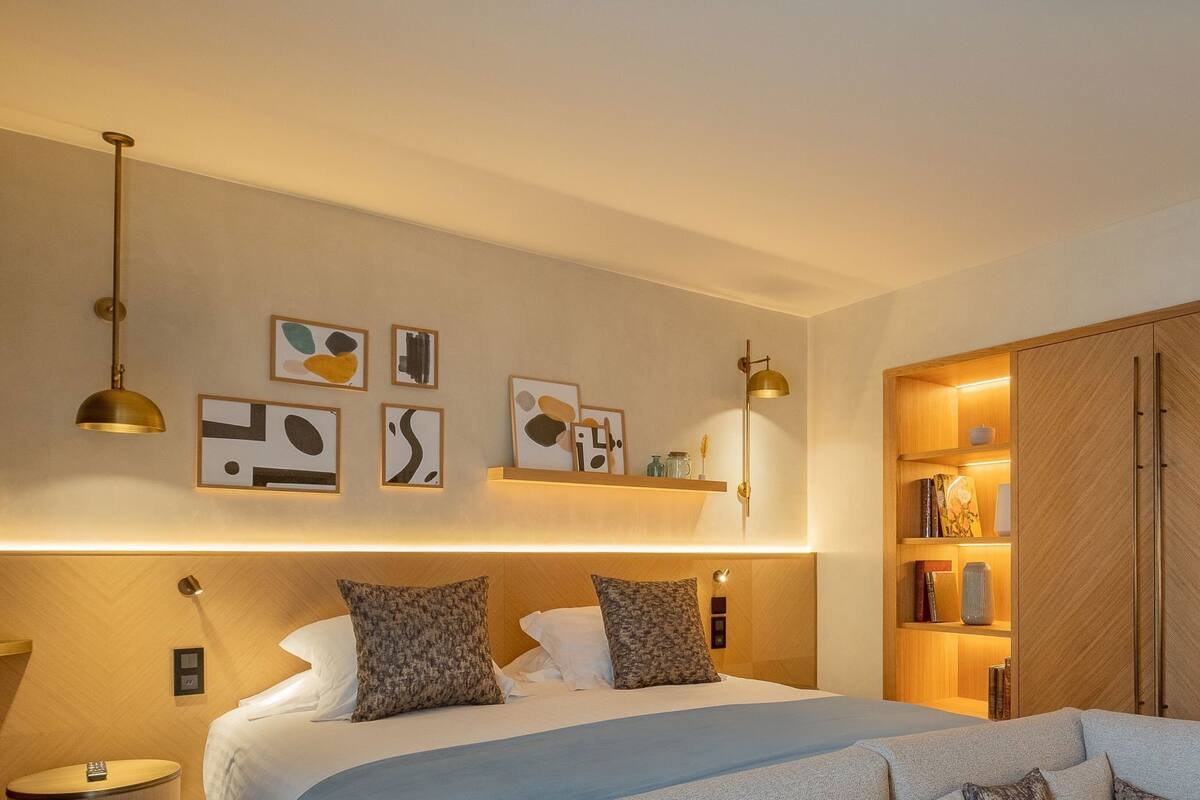 Ein modernes Hotelzimmer mit Bett, Nachttischlampen, einem Kleiderschrank und Wandbildern.