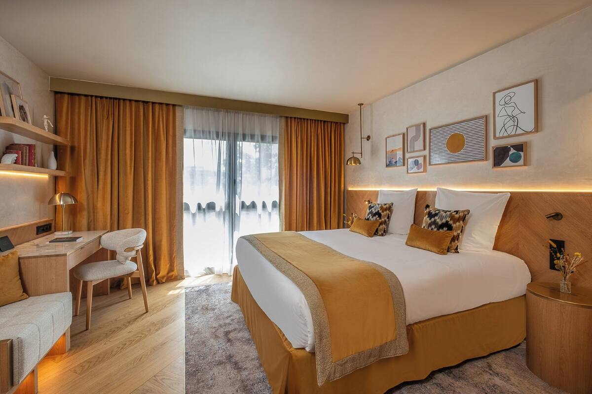 Ein modernes Hotelzimmer mit einem großen Bett, einem Schreibtisch und einem Sessel. Vorhanden sind Vorhänge, ein Fenster und Wandbilder.