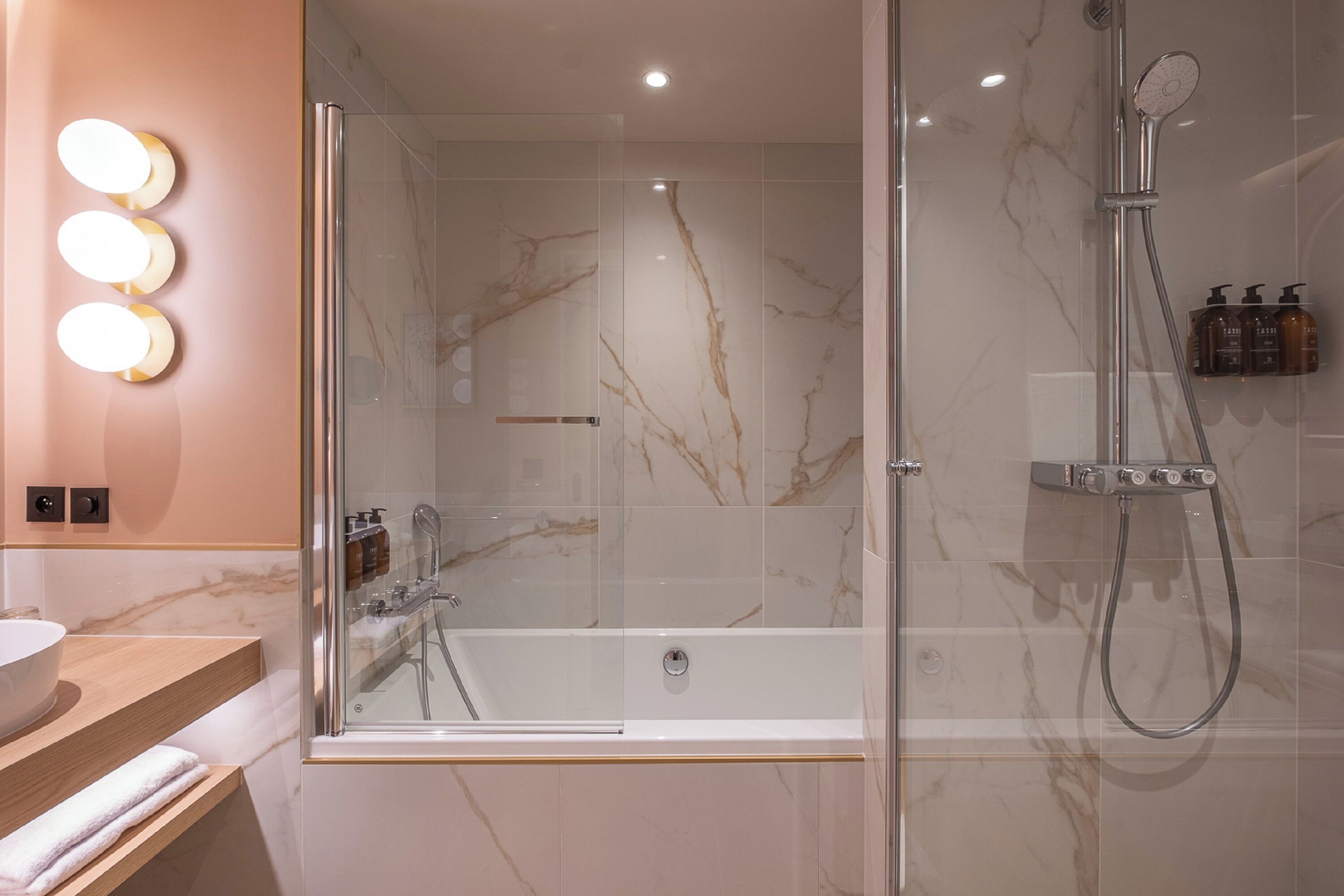 A modern bathroom with a glass-enclosed shower, a white bathtub, and a vanity with a mirror and lights.