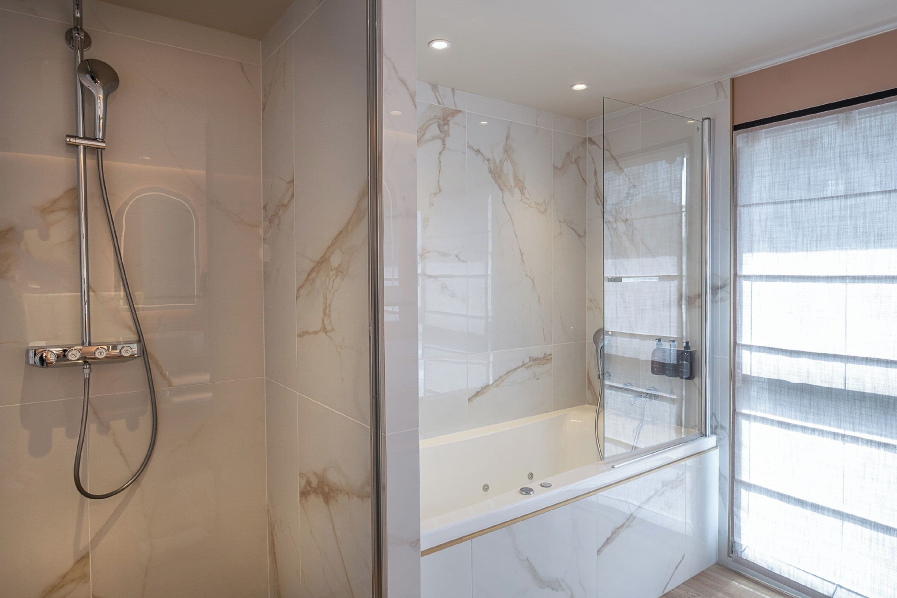 A modern bathroom with a glass-enclosed shower, a bathtub, and marble walls.