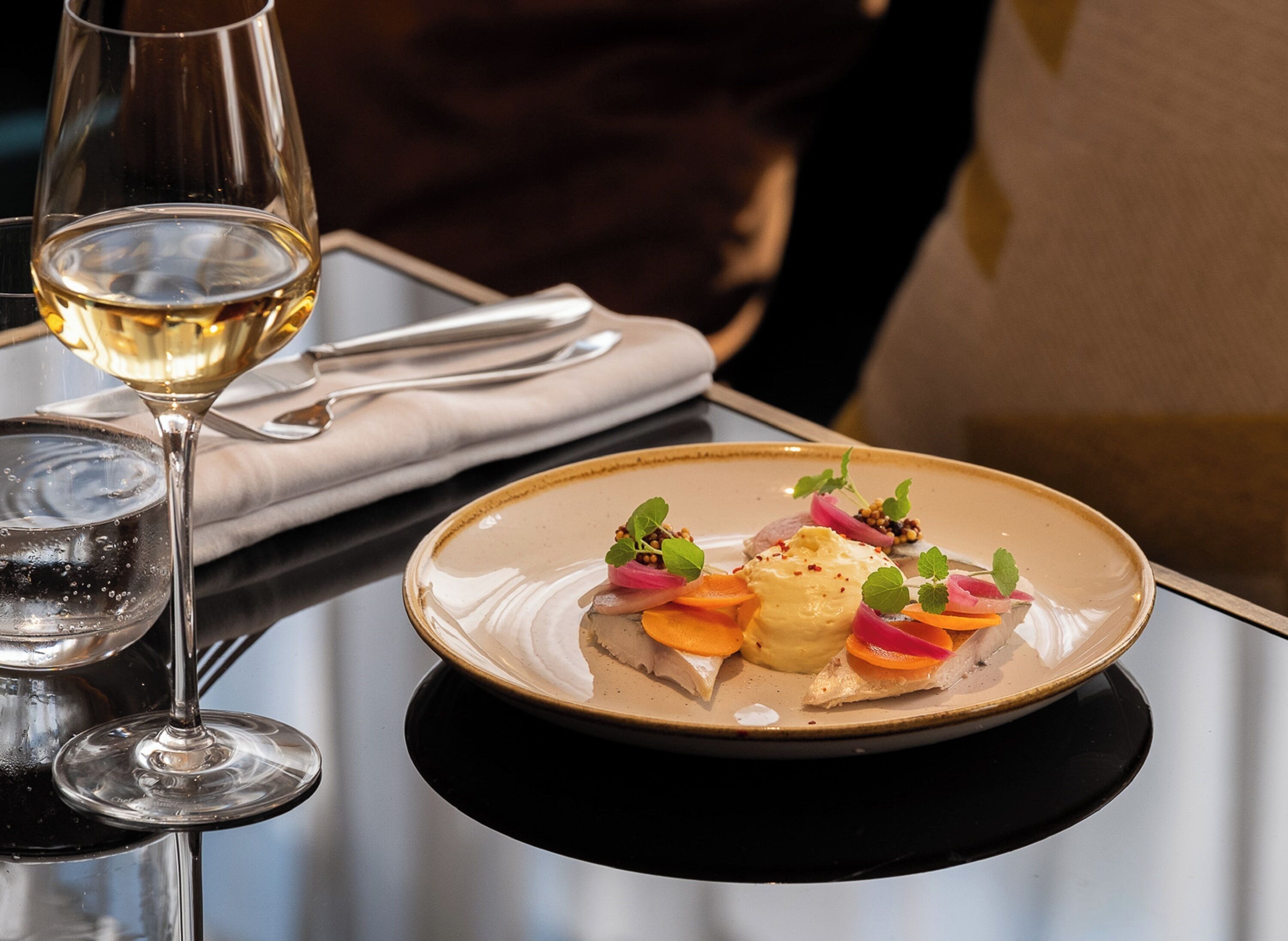 Una mesa de comedor con un plato de comida y una copa de vino blanco.