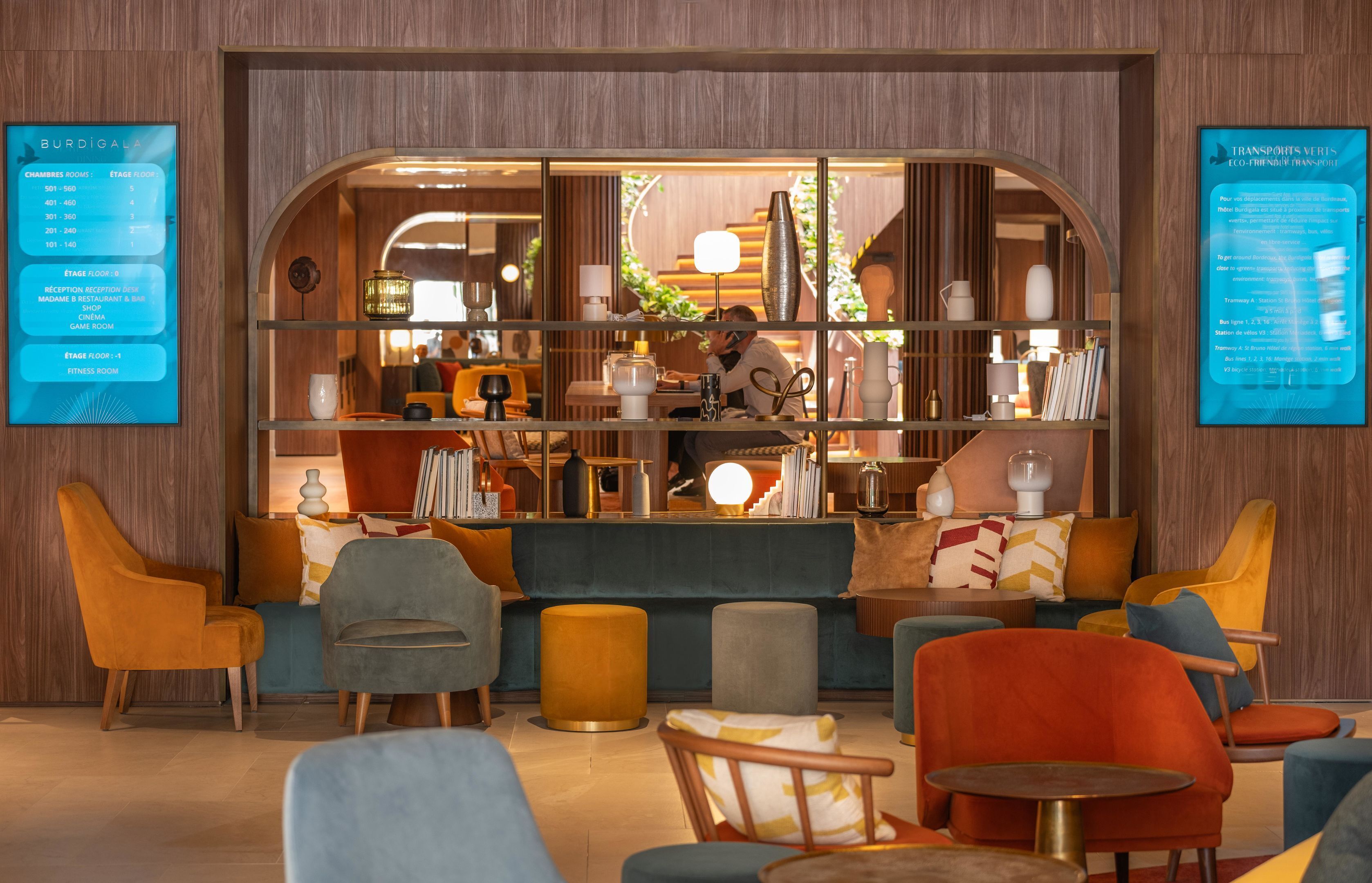 Un hall d’entrée moderne doté d’espaces de détente, d’un comptoir d’accueil et offrant une vue sur le restaurant.