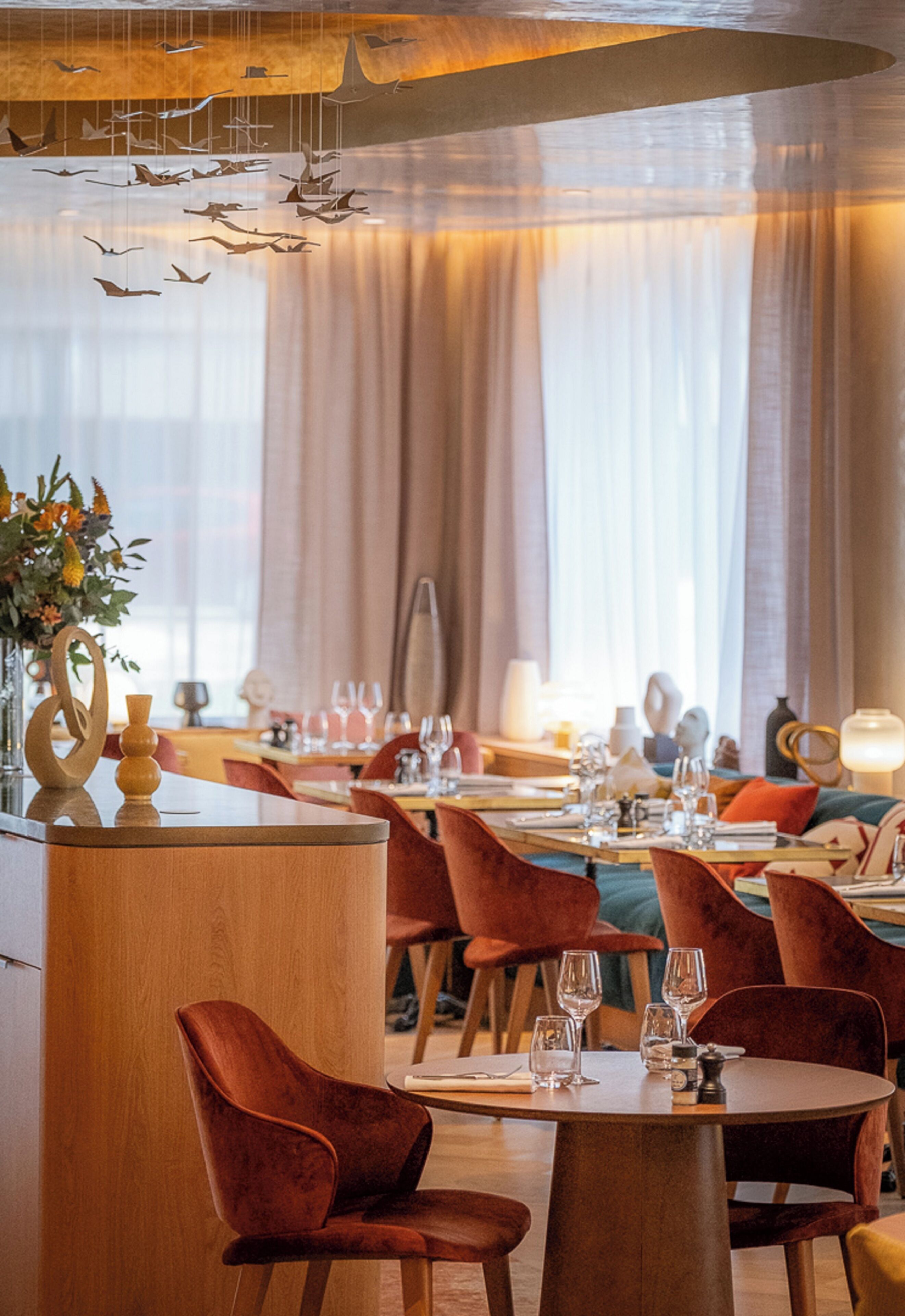 A restaurant with round tables, red velvet chairs, and hanging bird decorations.
