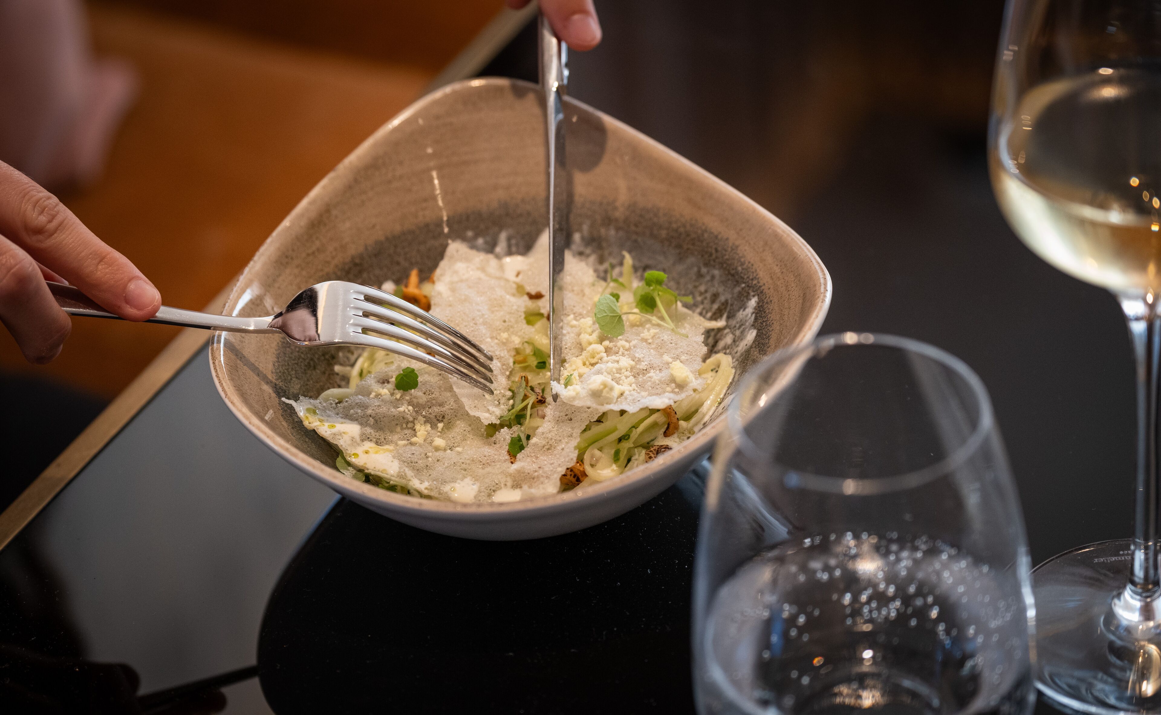 Un plato de comida con un tenedor, un vaso de agua y una copa de vino sobre una mesa.