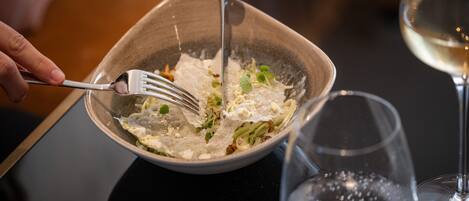 A bowl of food with a fork, a glass of water, and a glass of wine on a table.