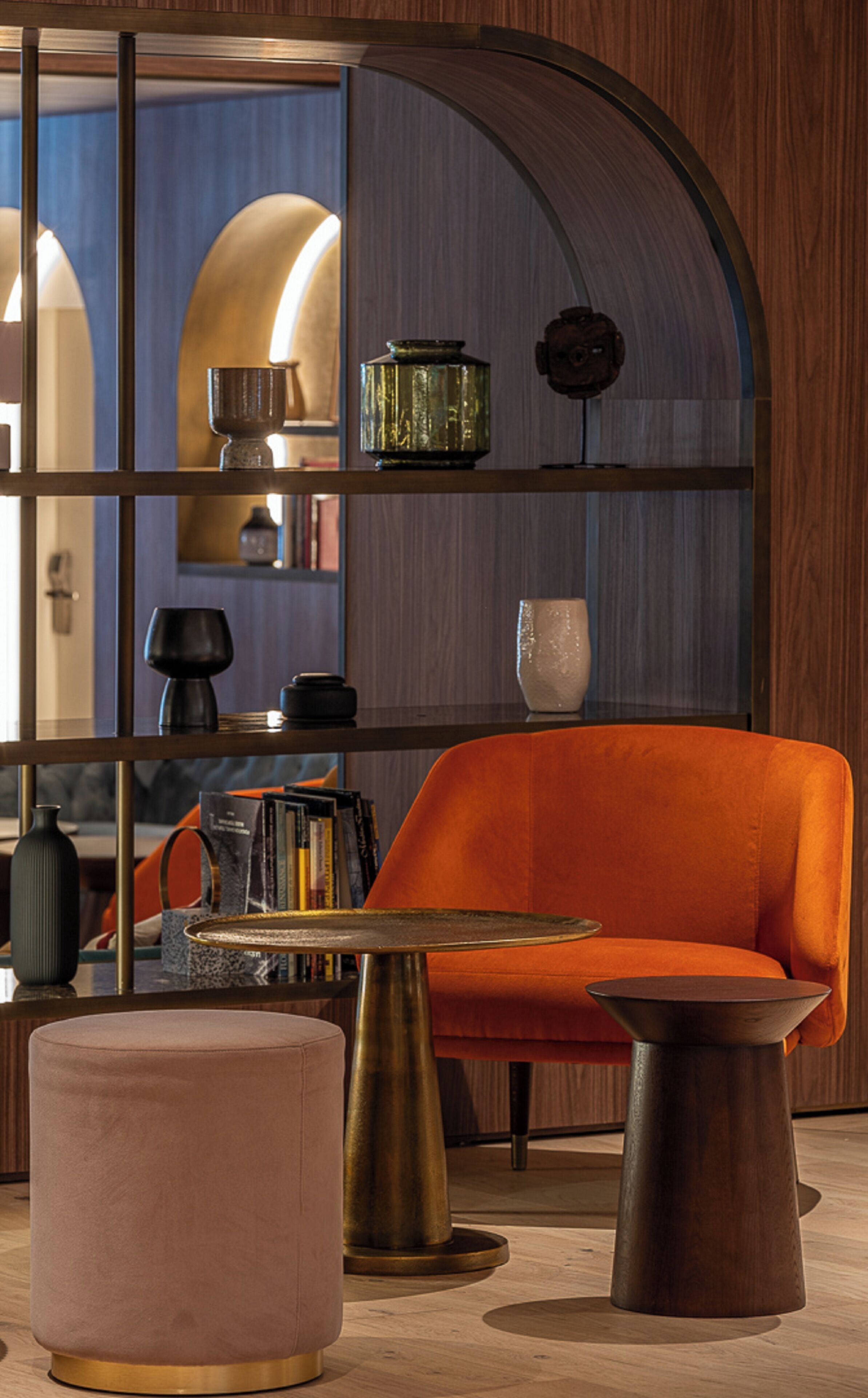 Un interior moderno con una pared curva de madera, un sofá naranja vibrante, una mesa redonda y un otoman rosa.