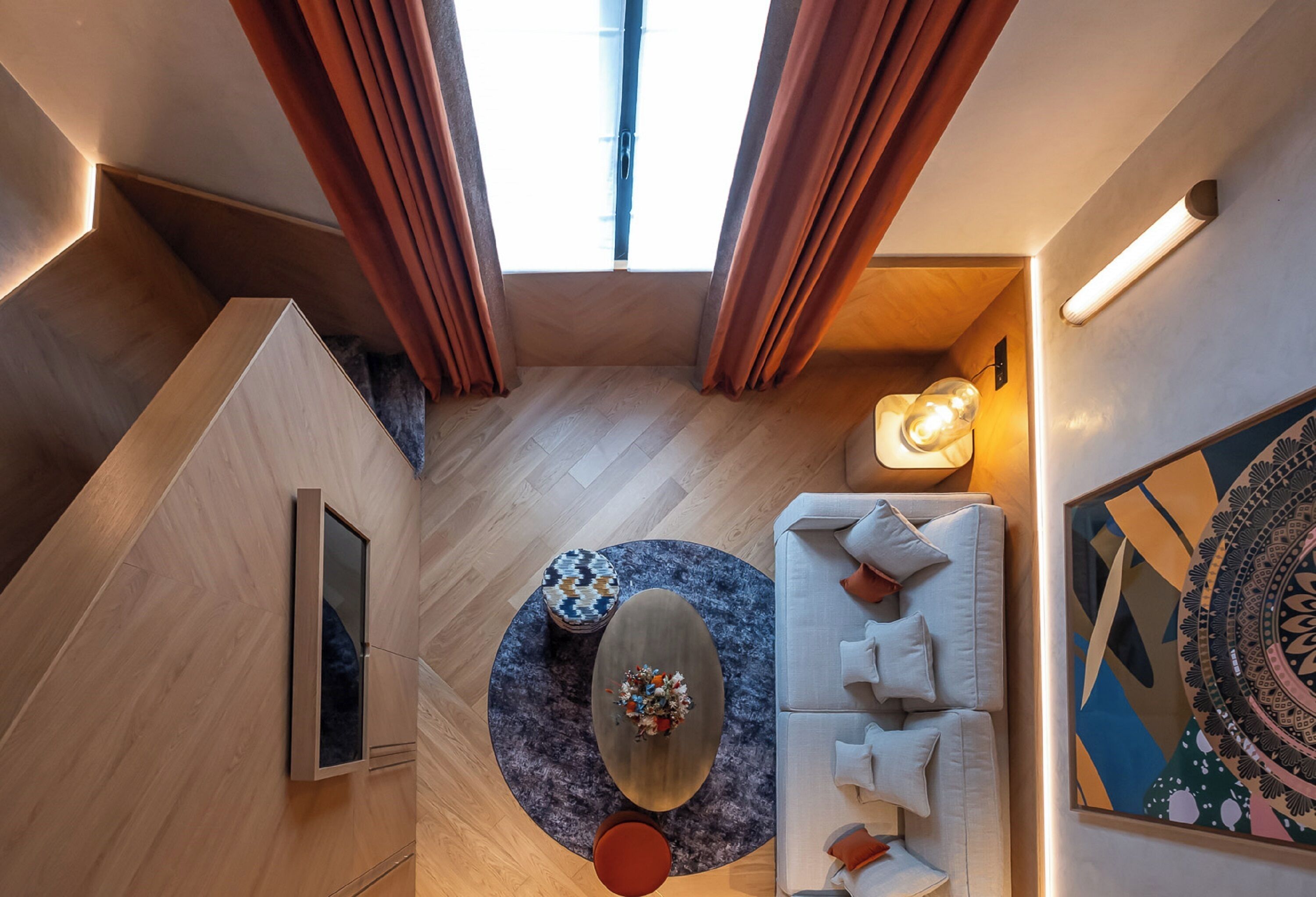 Un intérieur moderne avec un plancher en bois, une table basse ronde, un canapé avec des coussins, un téléviseur et une grande fenêtre avec des rideaux.