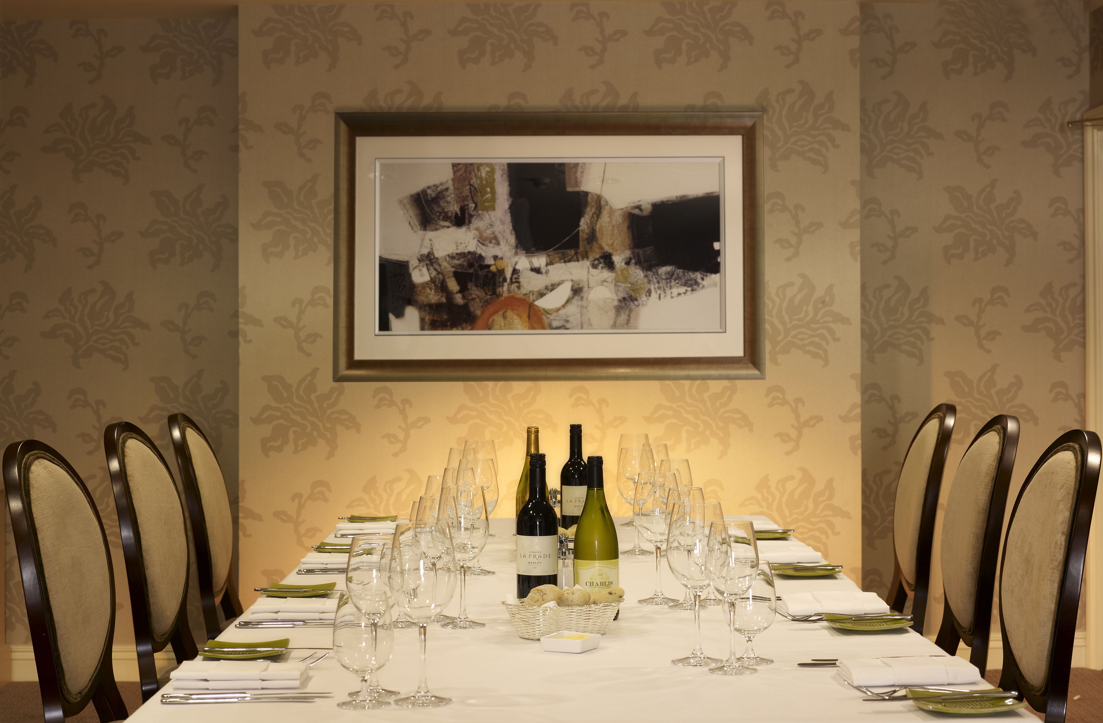 Una mesa de comedor dispuesta con botellas de vino, copas y platos, rodeada de sillas.