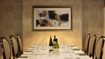 A dining table set with wine bottles, glasses, and plates, surrounded by chairs.
