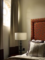 Una habitación de hotel con una cama, una lámpara, una ventana con cortinas y un cabecero estampado.