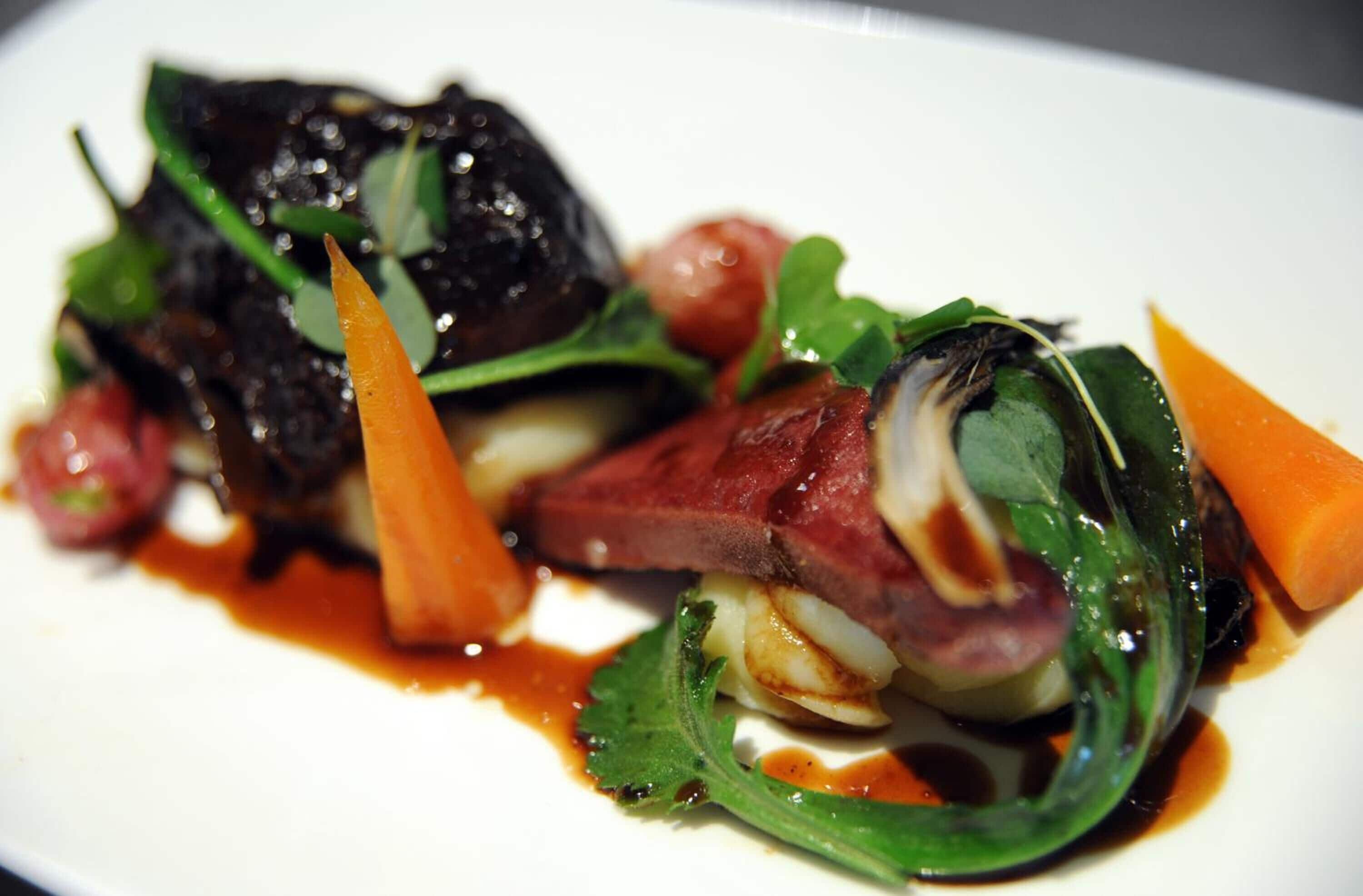 A close-up of a gourmet dish with various vegetables and meat.