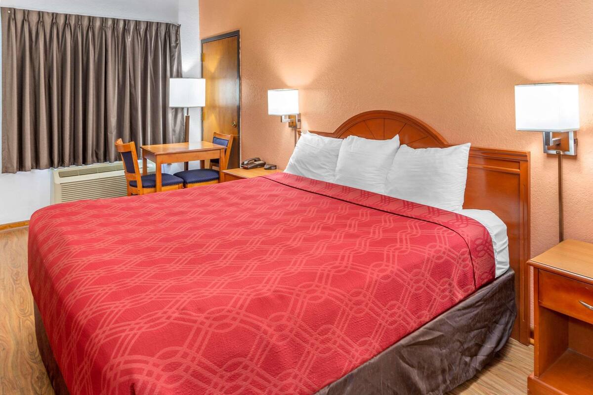 A hotel room with a large bed, two bedside lamps, a desk with a chair, and a window with curtains.