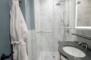 A modern bathroom with a white robe hanging on a towel rack, a glass shower enclosure, and a dark-toned sink with a mirror above it.