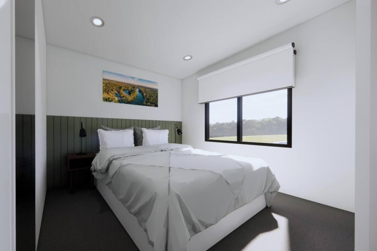 A modern hotel room with a large bed, a nightstand, a wall-mounted painting, and a window with a view.