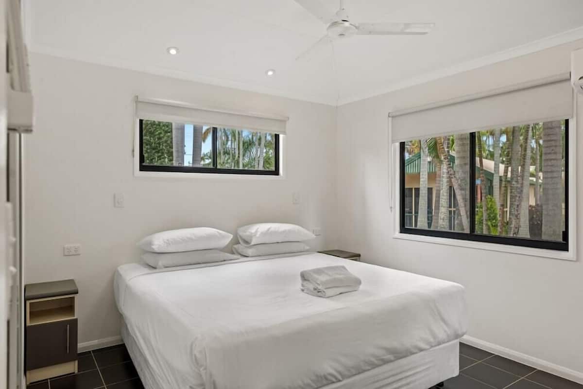 A bedroom with a bed, two windows, a ceiling fan, and a nightstand.