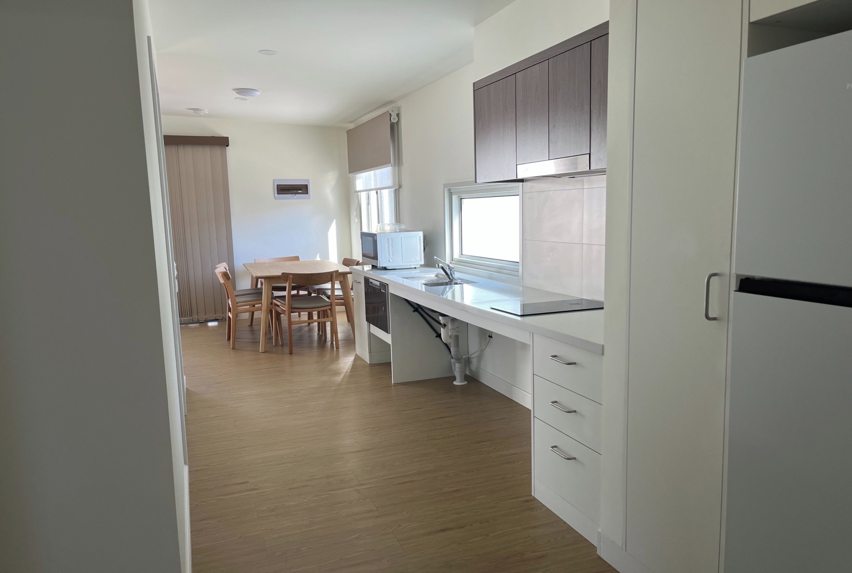 A modern kitchen with white cabinetry, a dining area with a wooden table and chairs, and a window providing natural light.