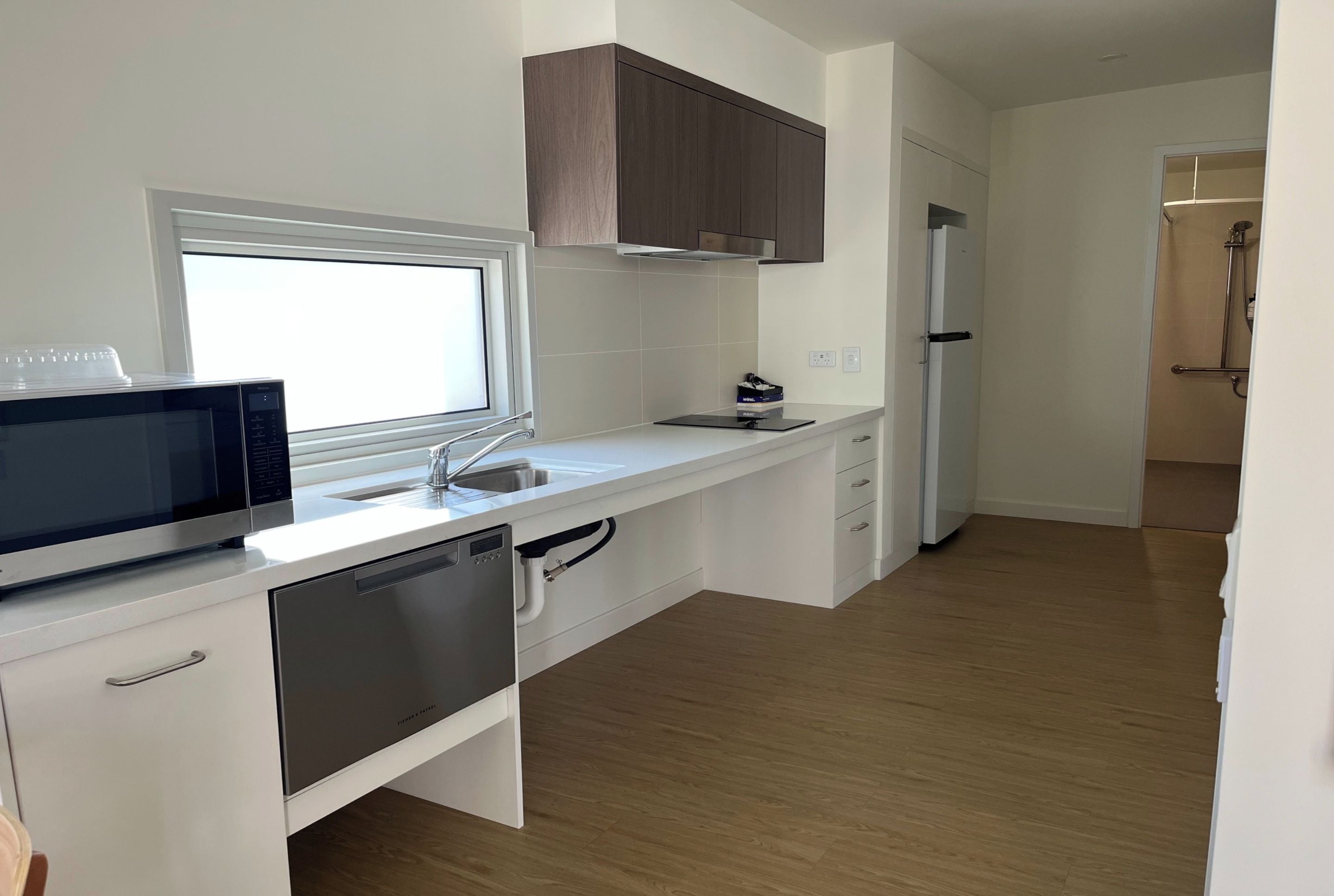 A modern kitchen with white cabinetry, a built-in dishwasher, a microwave, and a window above the sink.