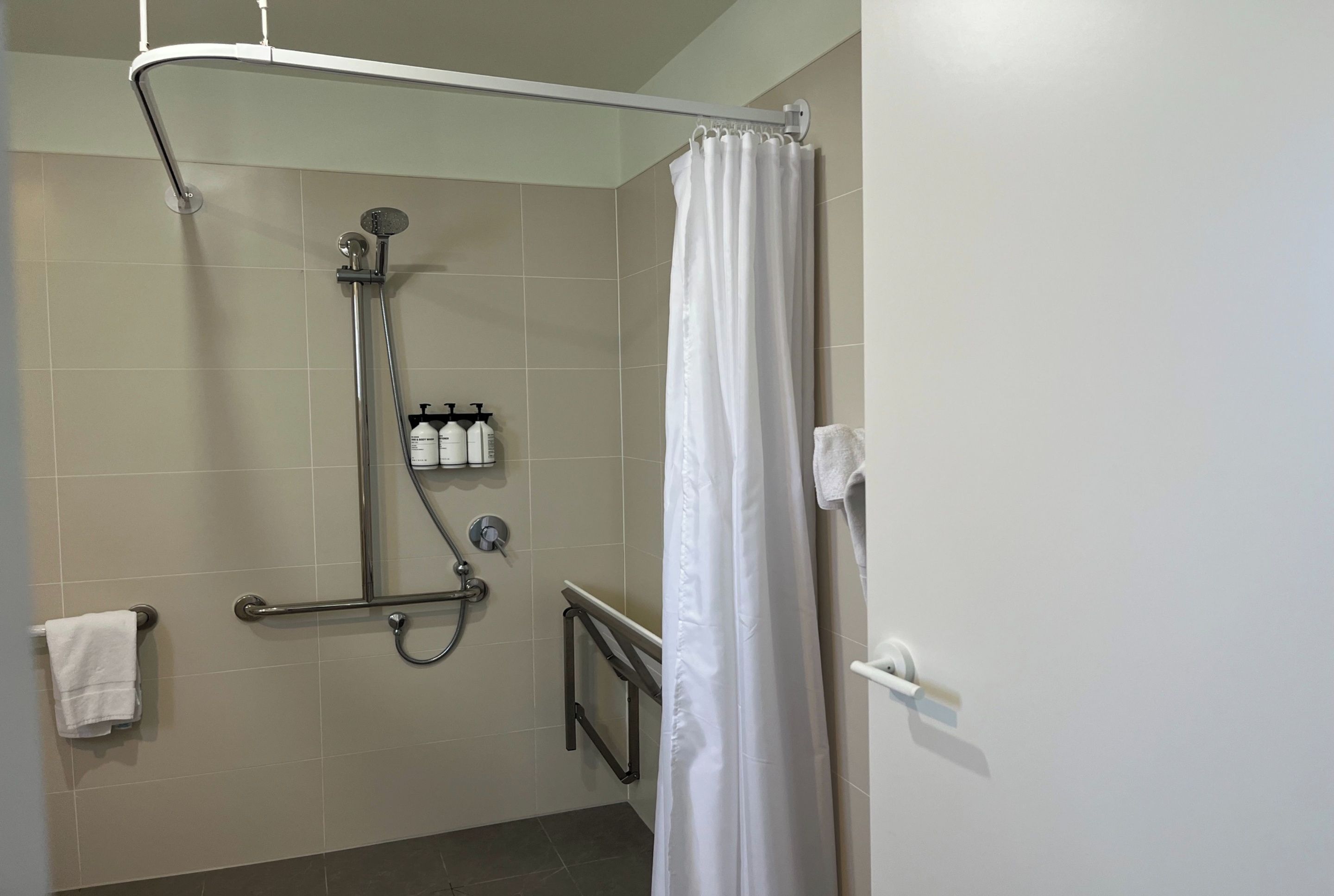 Zona de ducha con barra de apoyo, toallero y ducha.