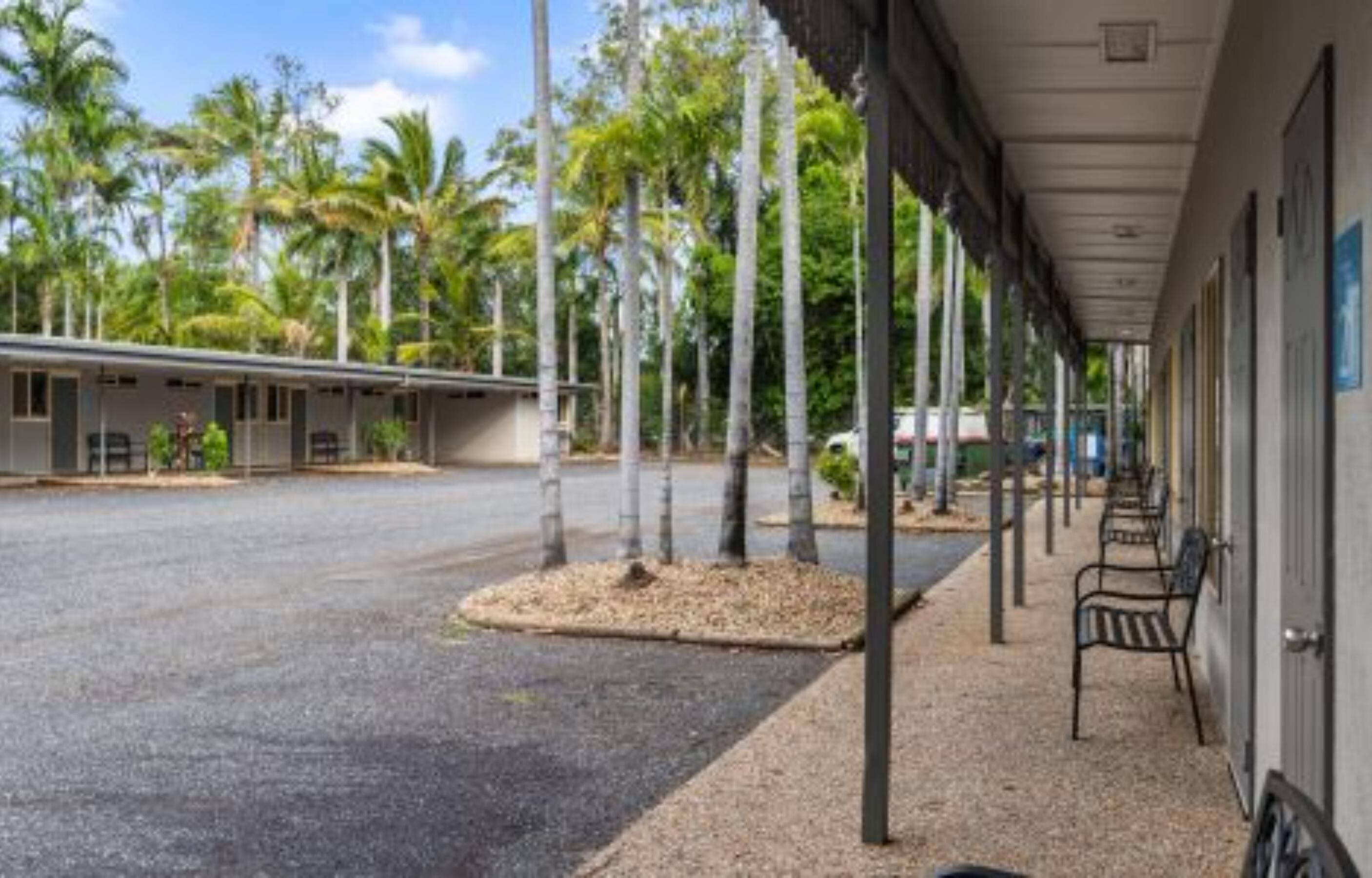 A motel with a covered walkway, palm trees, and a gravel parking area.