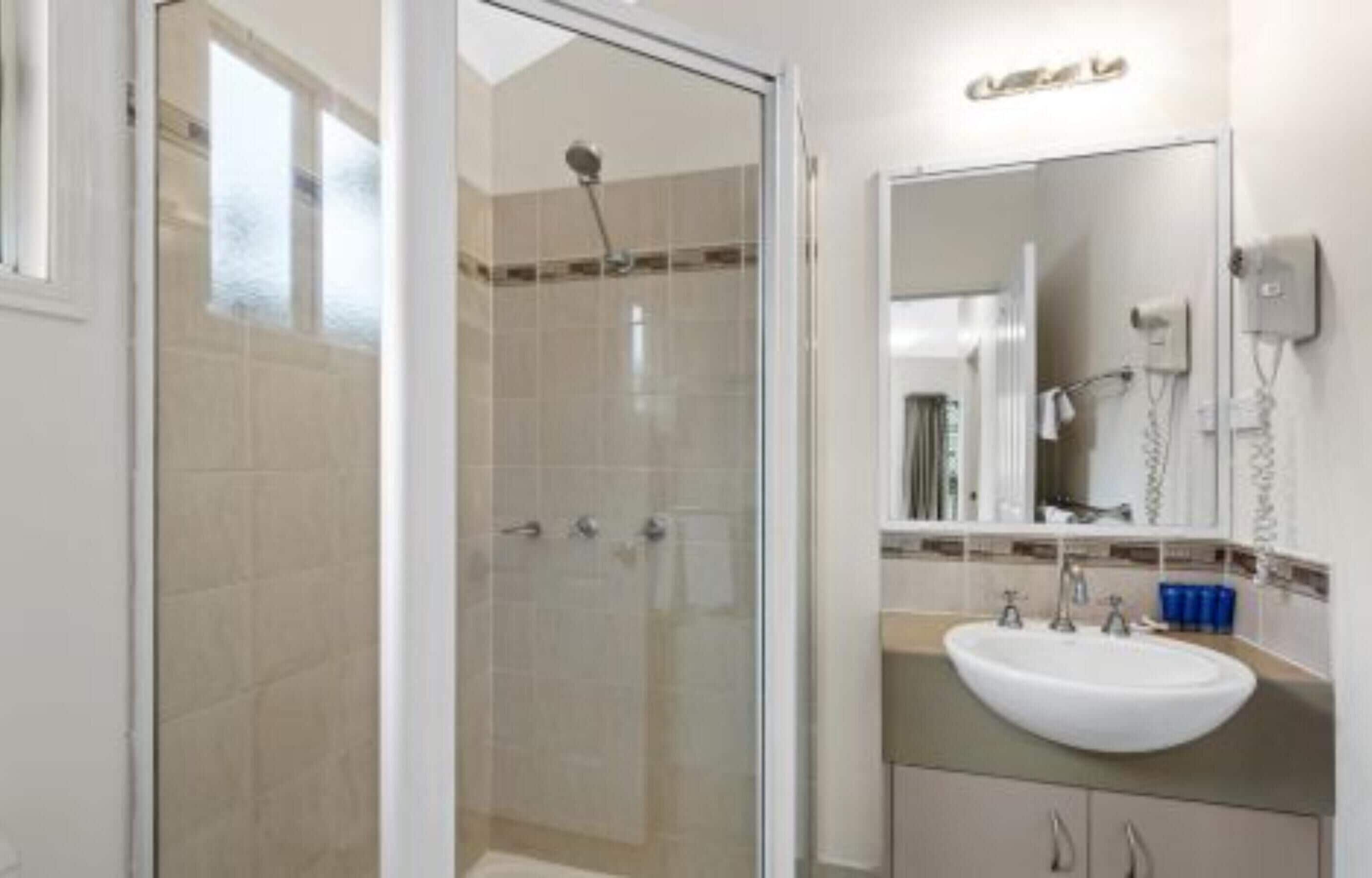 Un baño moderno con ducha de vidrio, lavamanos blanco y un espejo grande.