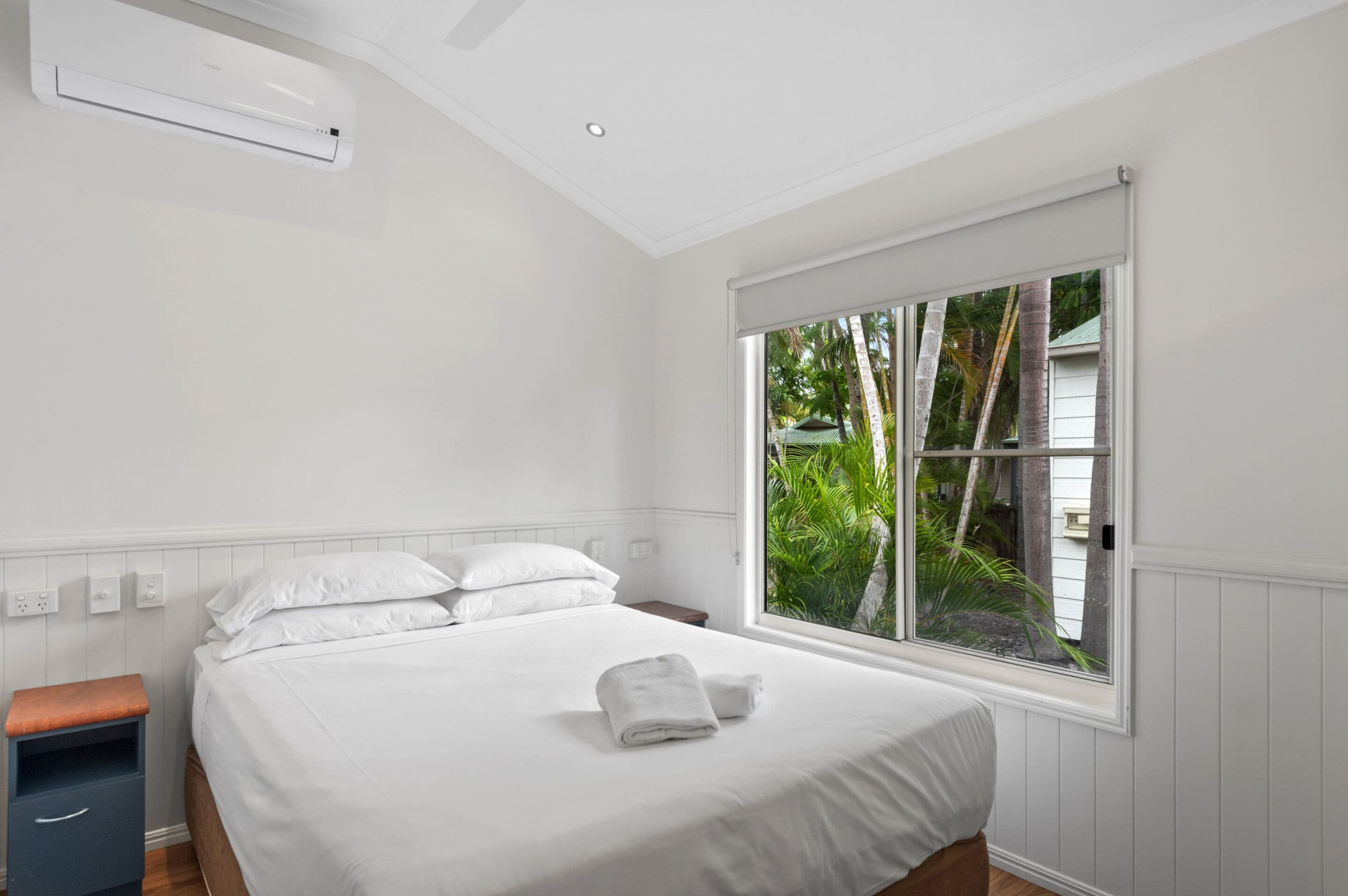 Un dormitorio con un ventanal grande, una cama, una mesita de noche y un aire acondicionado de pared.