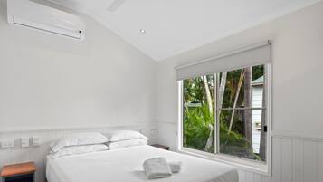 A bedroom with a large window, a bed, a nightstand, and a wall-mounted air conditioner.