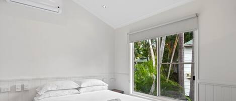 Un dormitorio con un ventanal grande, una cama, una mesita de noche y un aire acondicionado de pared.