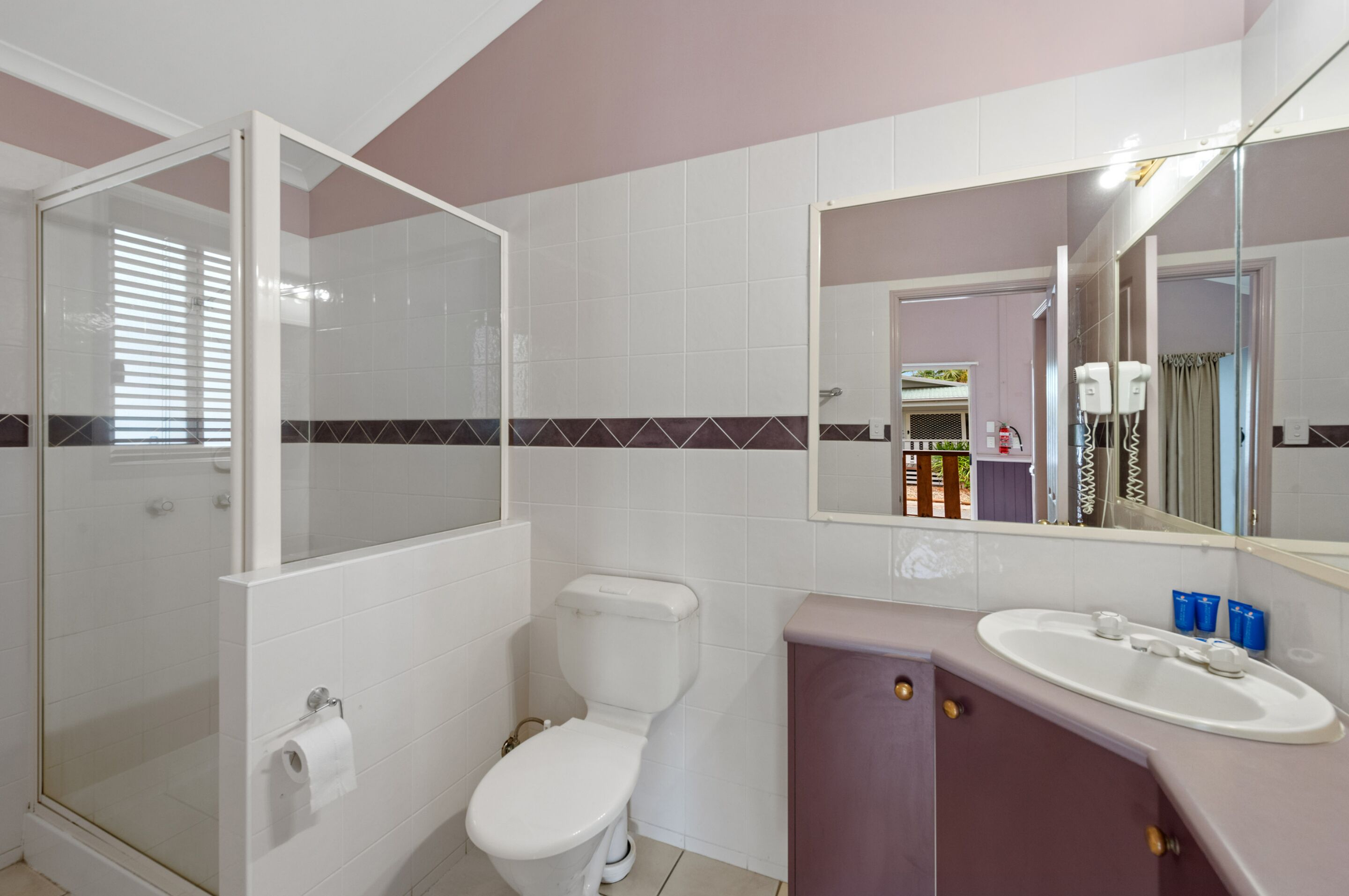 A bathroom with a glass-enclosed shower, a toilet, and a sink with a mirror above it.