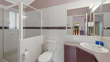 Un baño con ducha envuelta en vidrio, inodoro y lavamanos con espejo sobre él.