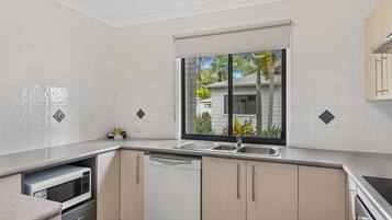 Cocina moderna con armarios blancos, lavavajillas, microondas y ventana con vista a una casa y palmeras.