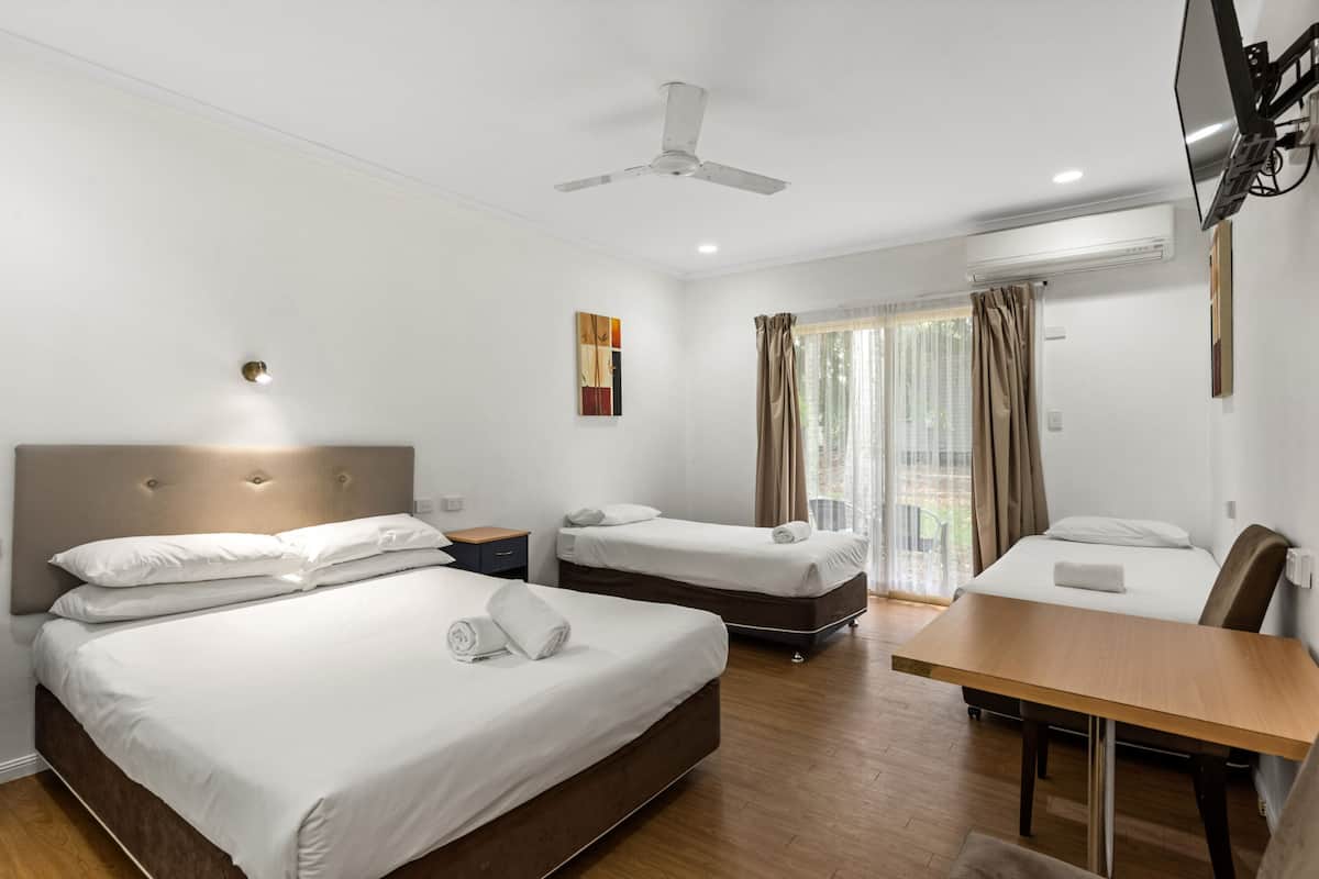 A hotel room with two beds, a desk, a ceiling fan, and a TV mounted on the wall.