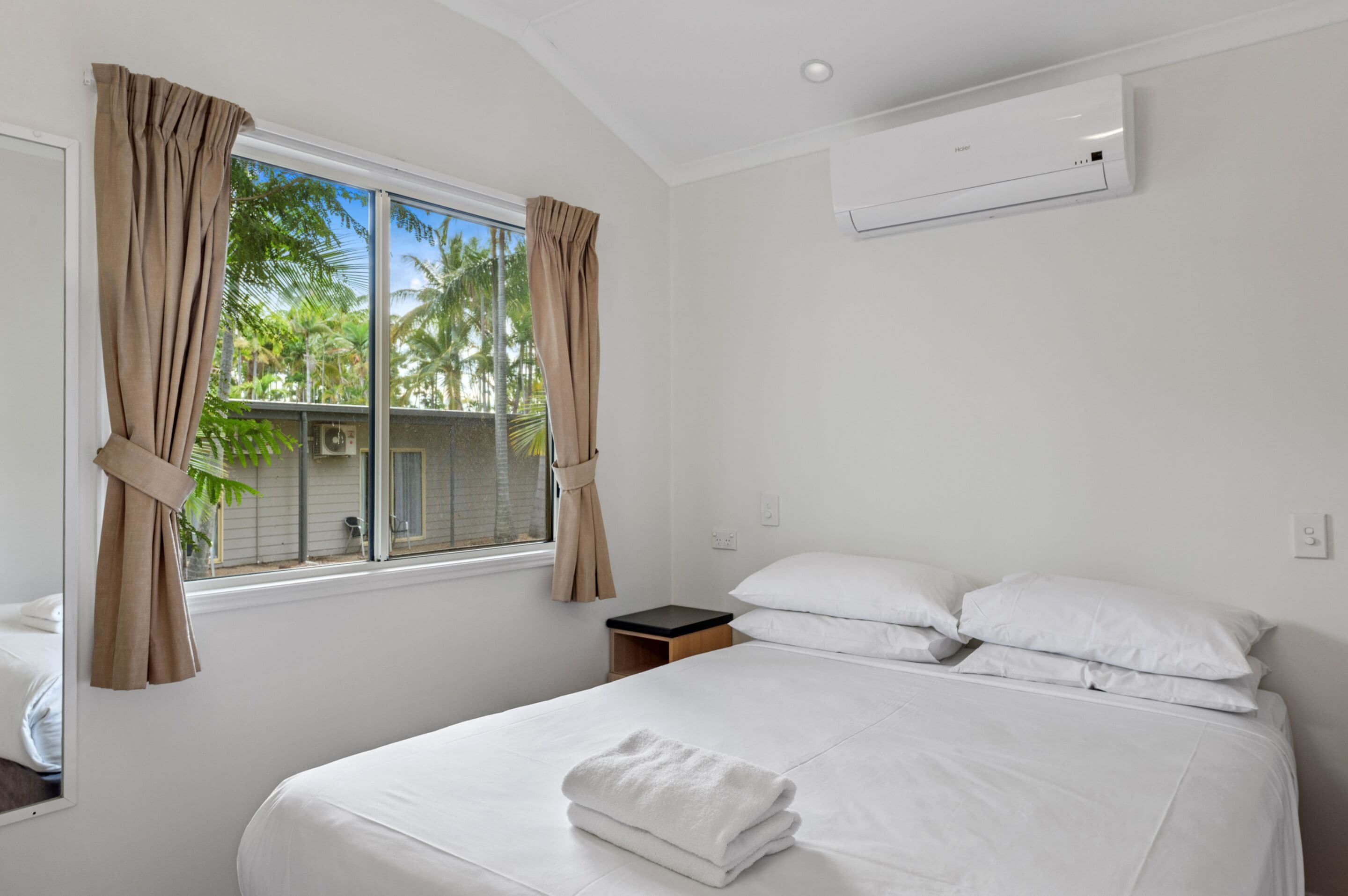 Habitación de hotel con cama, ventana con cortinas, mesita de noche y equipo de aire acondicionado.