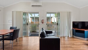 A modern living room with a wooden dining table, black leather sofa, and a flat-screen TV. - Discovery Parks - Rockhampton (Norman Gardens)