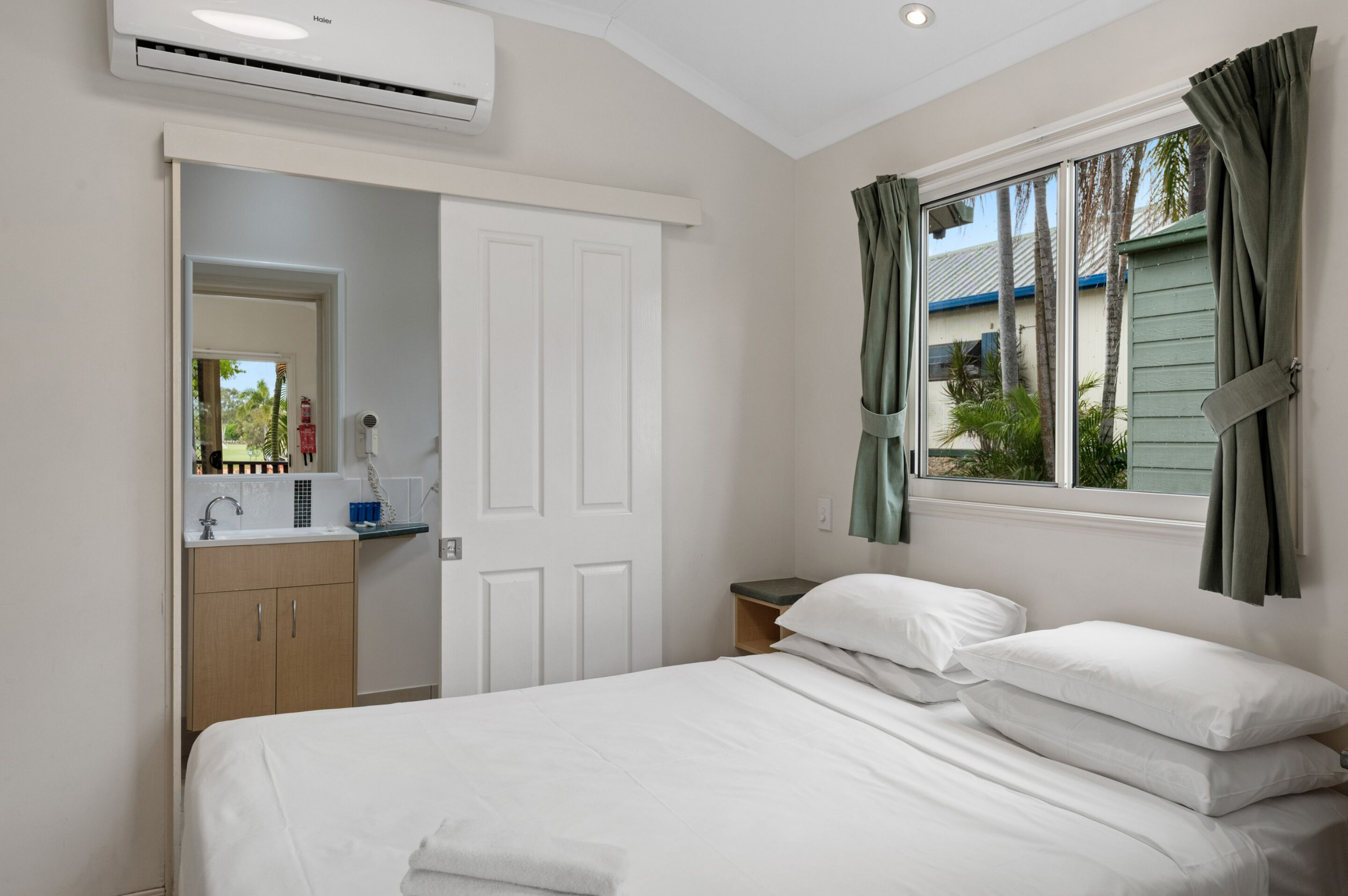 A hotel room with a bed, a bathroom with a sink, and a window with curtains.