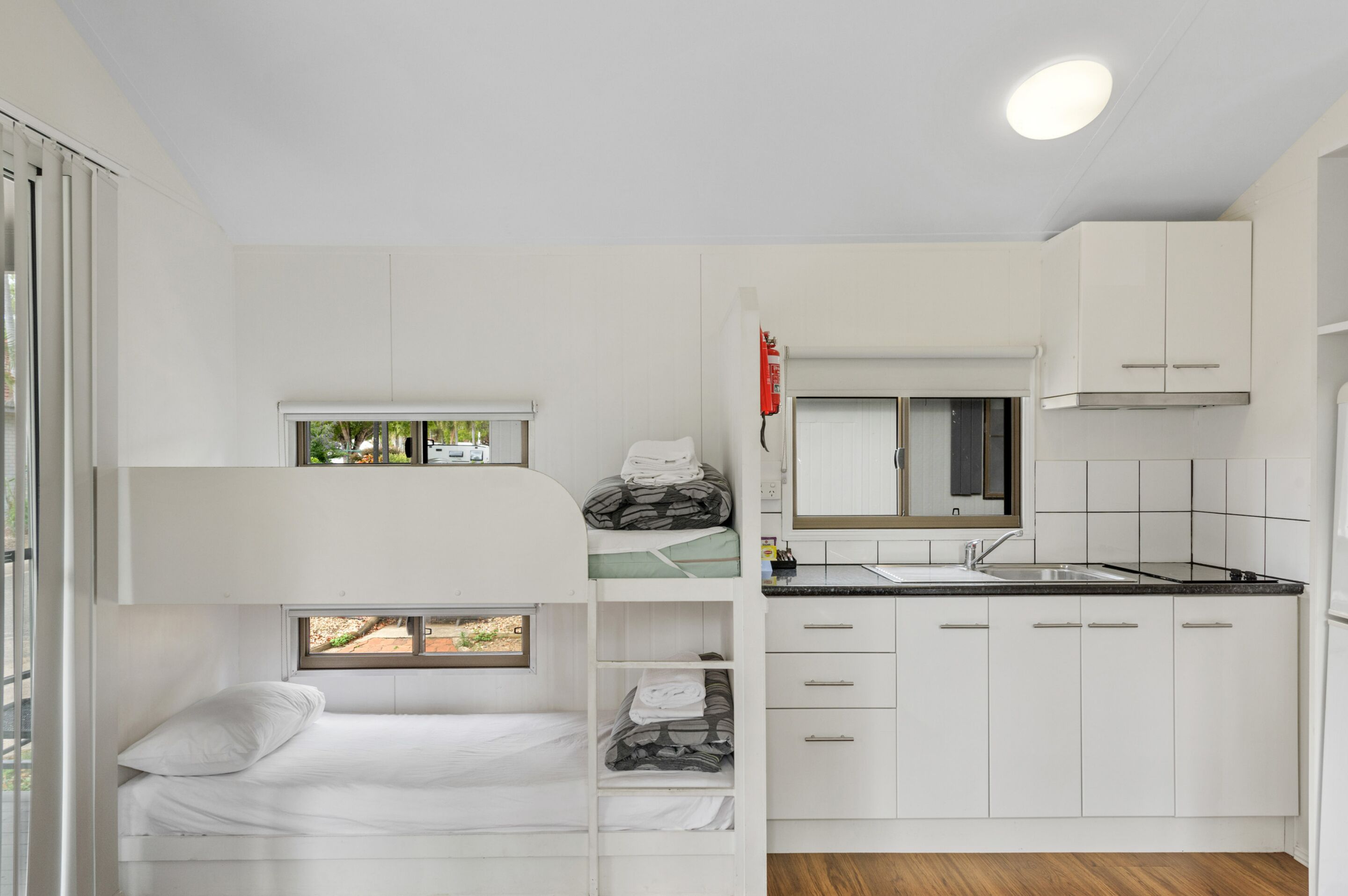 A compact, modern room with bunk beds, a kitchenette, and a window providing natural light.