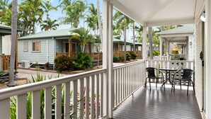 A covered outdoor area with a wooden deck, white railings, and a seating area with chairs and a table. - Discovery Parks - Rockhampton (Norman Gardens)