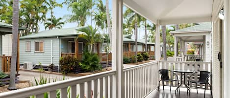 A covered outdoor area with a wooden deck, white railings, and a seating area with chairs and a table.