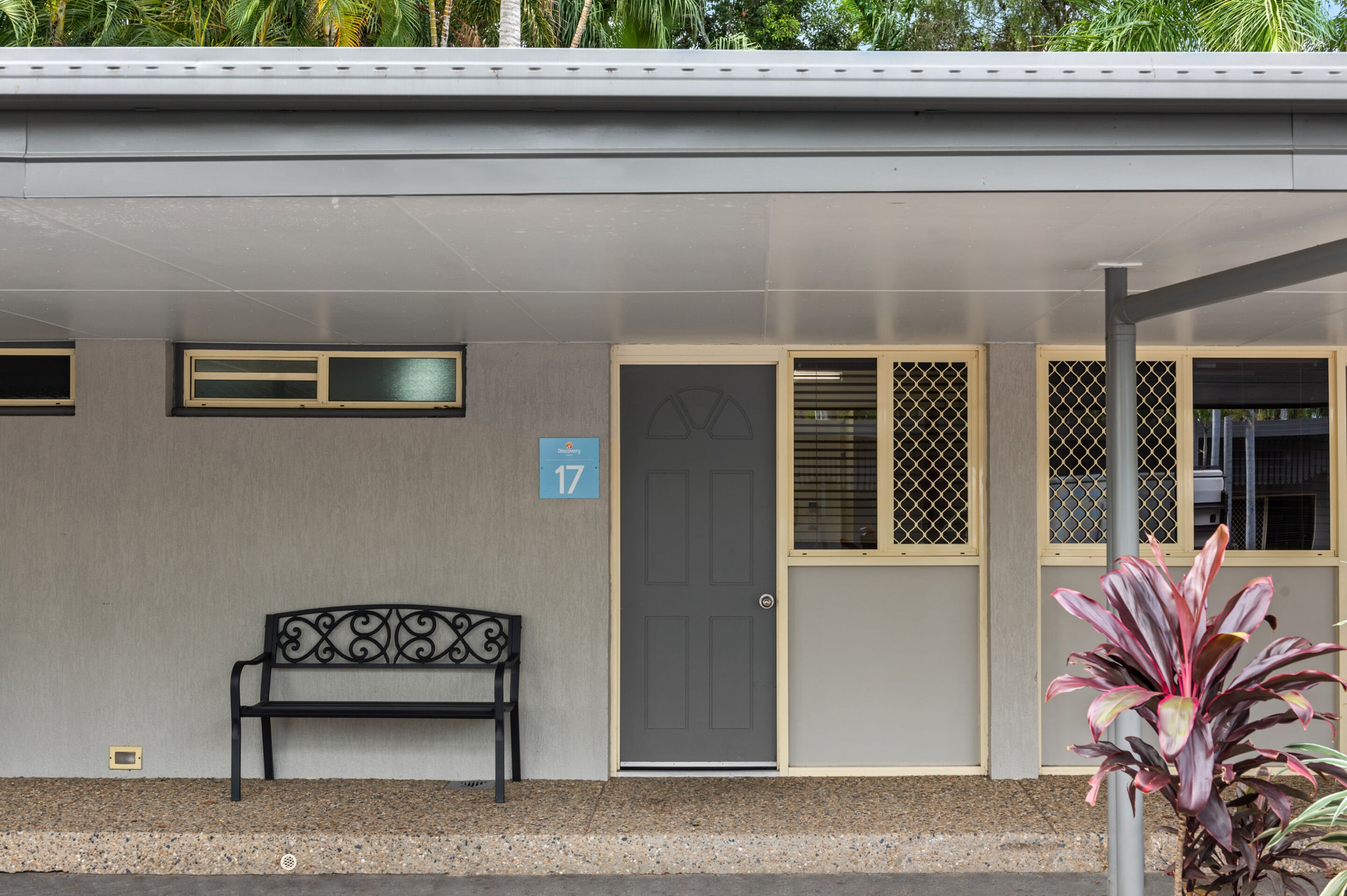 A building with a grey facade, a door with a number 17 sign, a bench, and a potted plant.