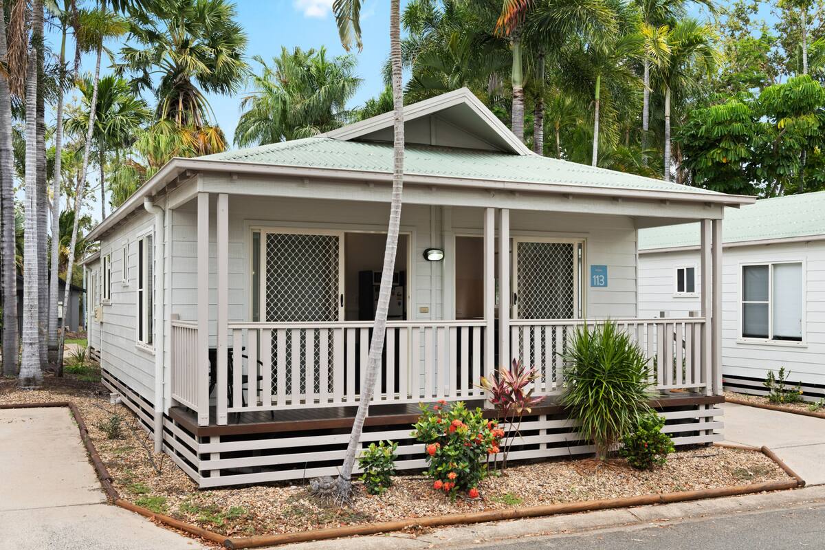 A single-story house with a porch, surrounded by palm trees.