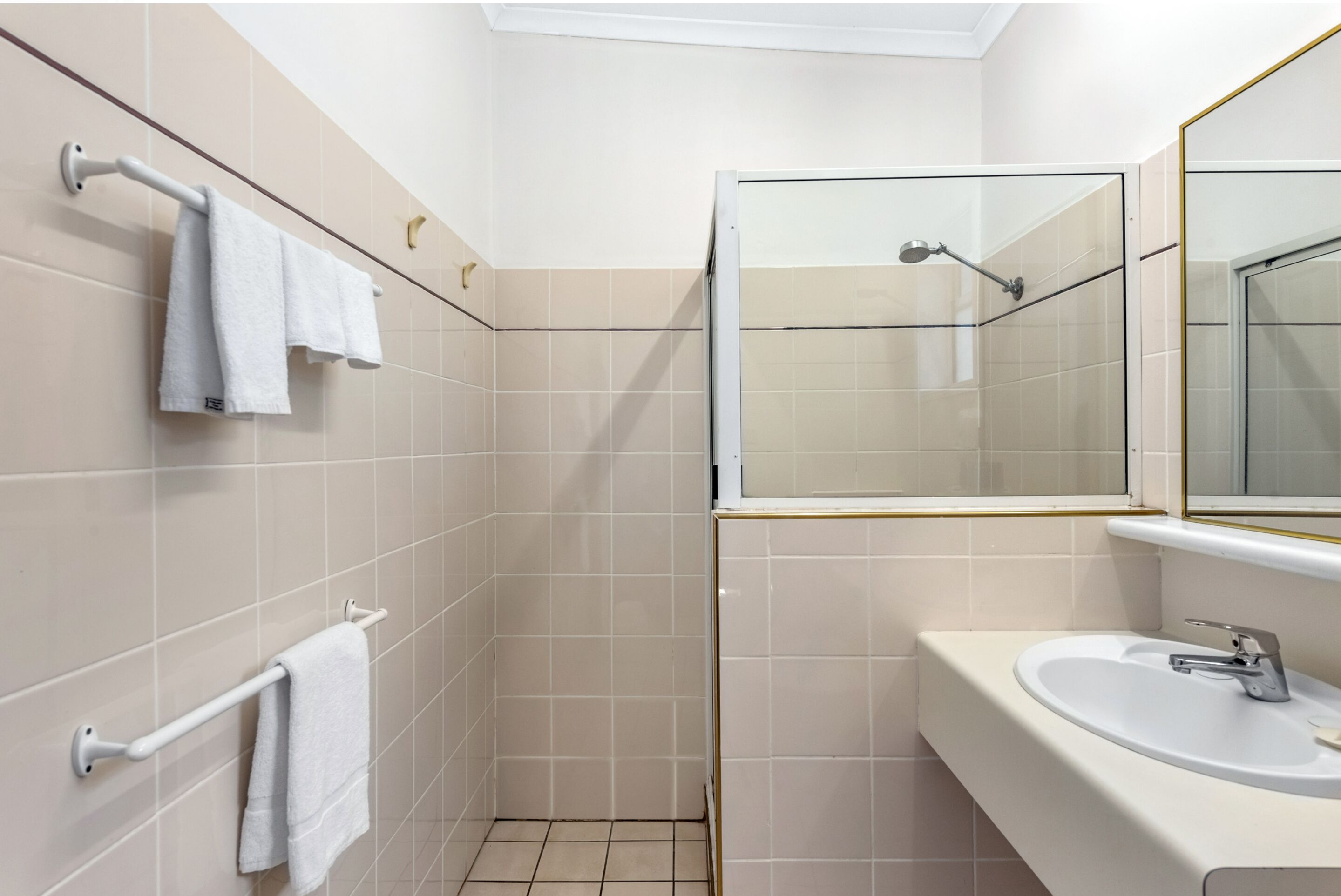 A bathroom with beige tiles, a white sink, and a glass-enclosed shower.