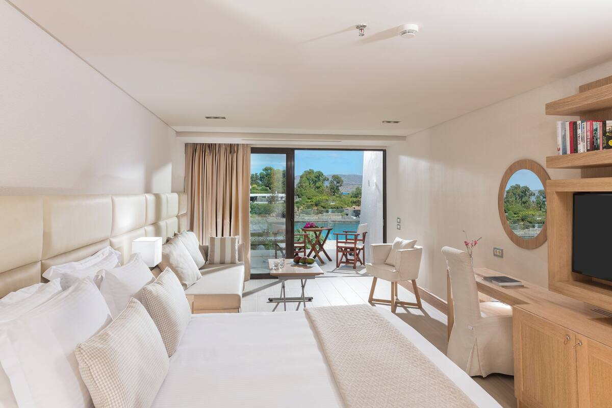 Habitación de hotel moderna con una cama grande, un escritorio, un televisor y un balcón con vista a la piscina.