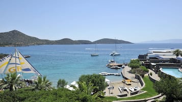 A coastal hotel with a pool, boats, and a clear view of the sea.