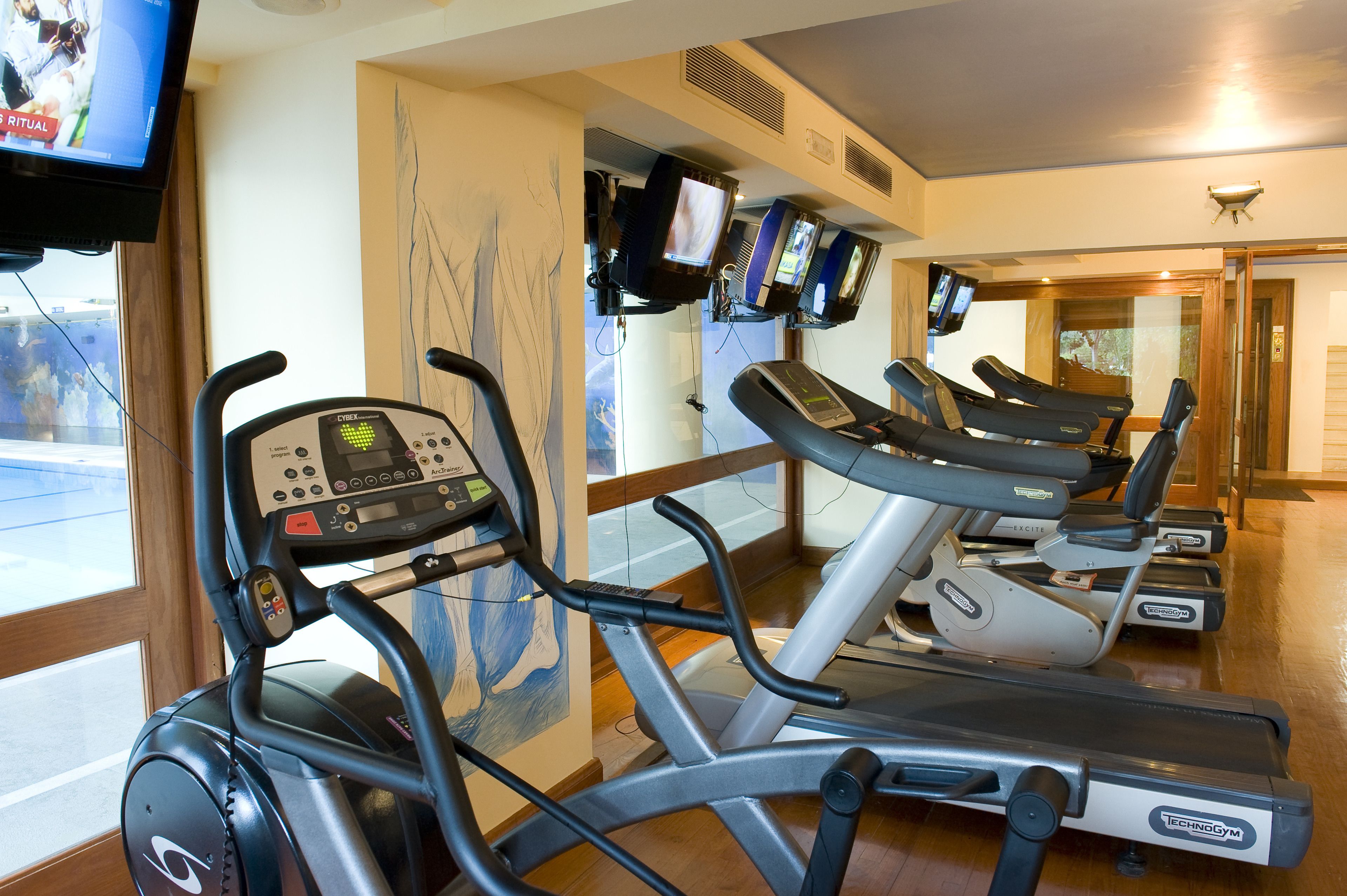 A gym with treadmills, stationary bikes, and a TV screen displaying a workout video.