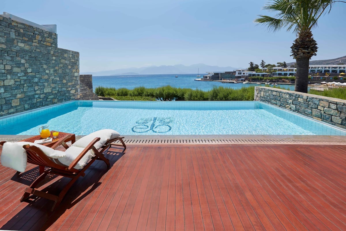 Un área junto a la piscina con terraza de madera, sillas de descanso y vista al mar.
