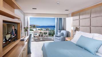 A modern hotel room with a large bed, a TV, a desk, and a balcony with a view of the sea.